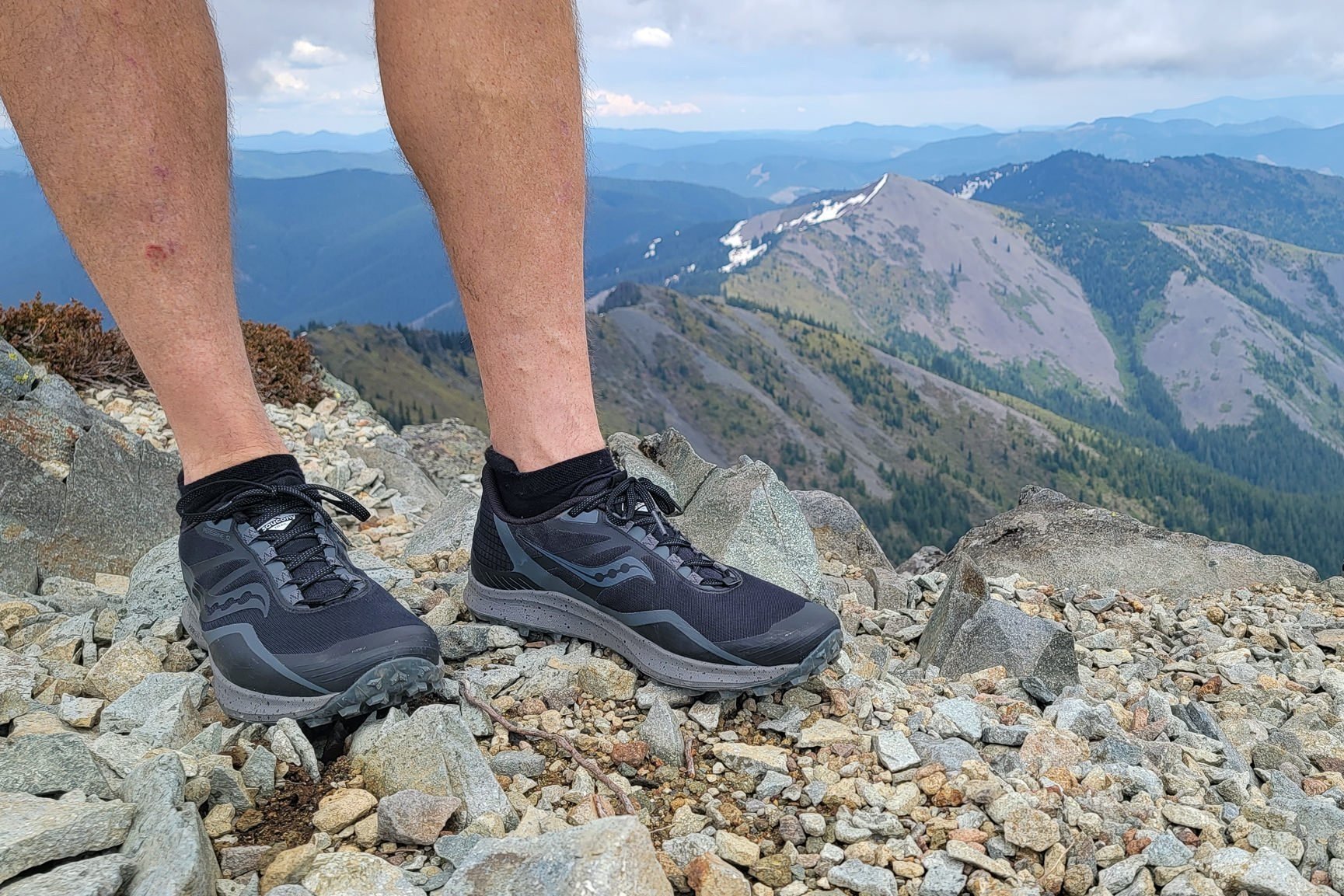 Closeup of a backpacker wearing a pair of black Saucony Peregrine trail running shoes on a mountain ridge