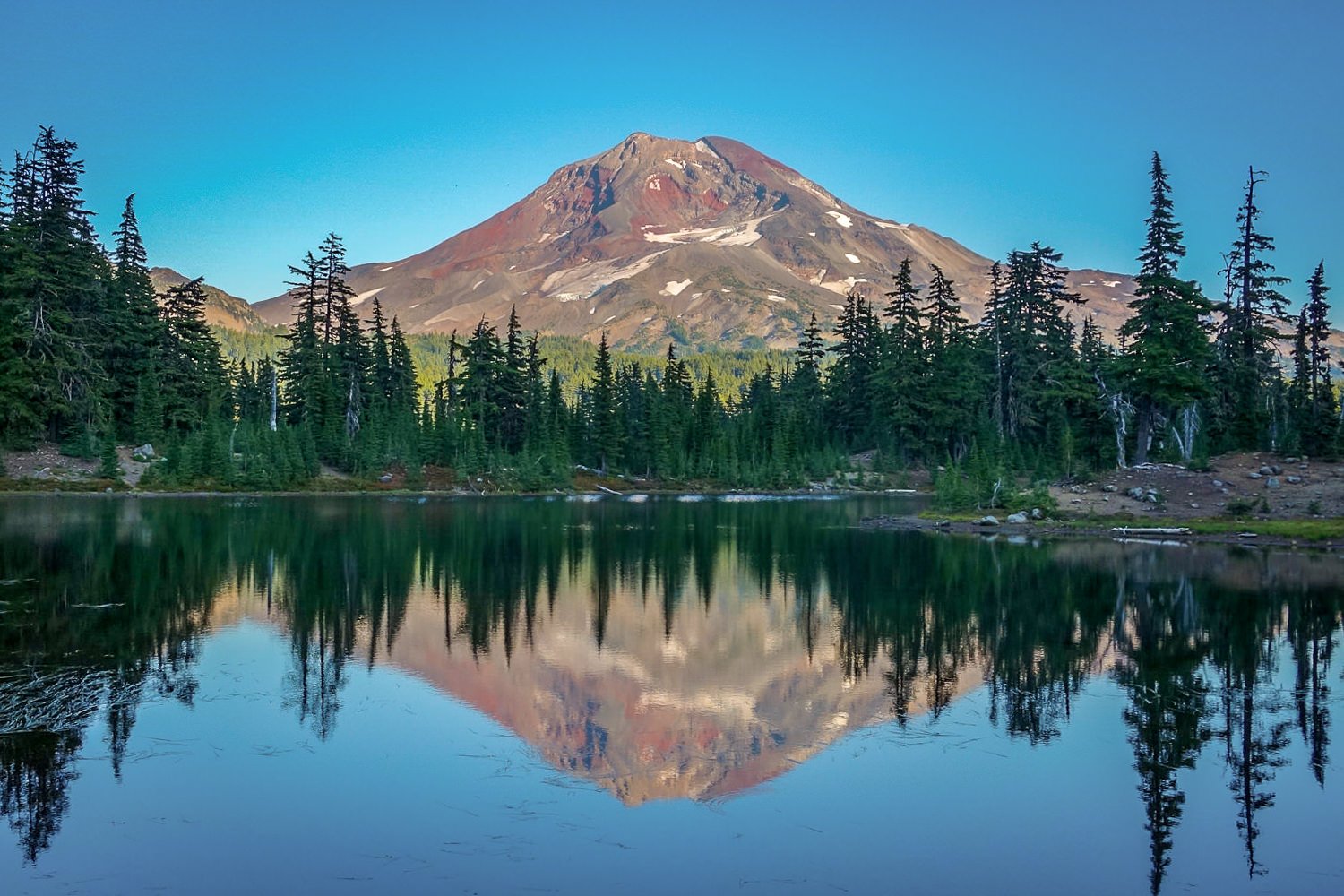 A view of South Sister from across a tree-lined lake.