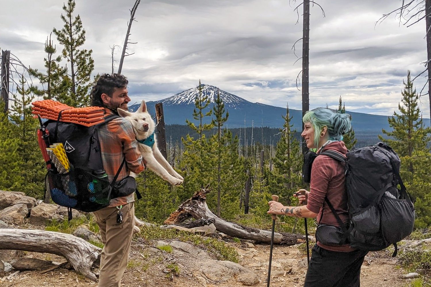 A backpacker holding a dog in front of Mt. Bachelor;