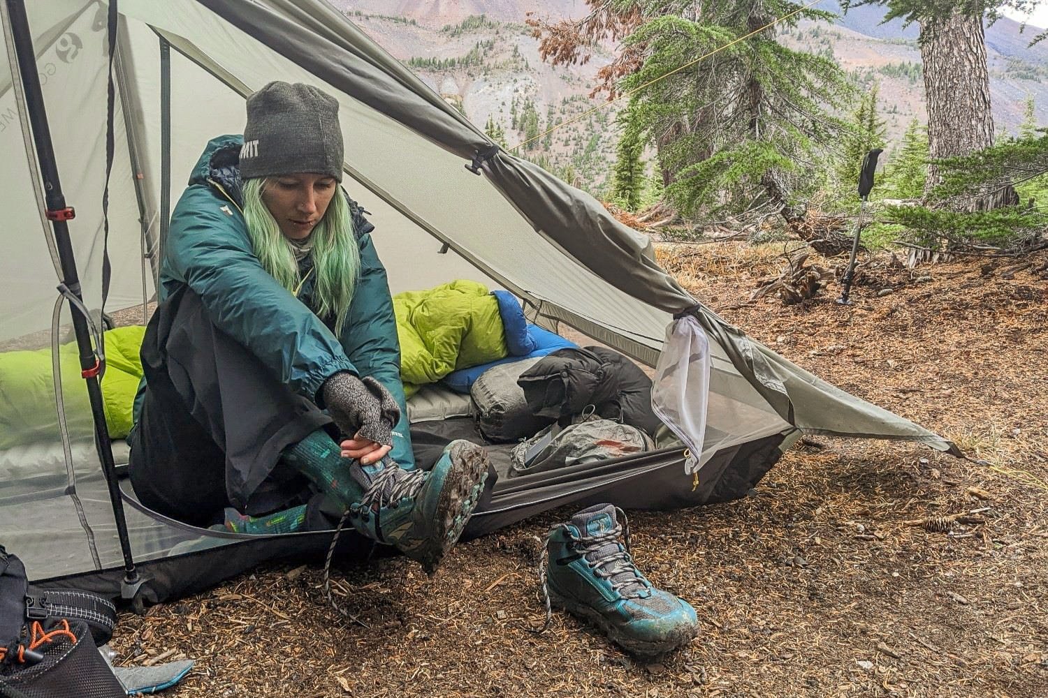 A backpacker putting on her shoes in the door of her backpacking tent.