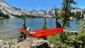 A backpacker relaxing in a red Eno Ultralight Sub6 hammock near a mountain lake in the Enchantments