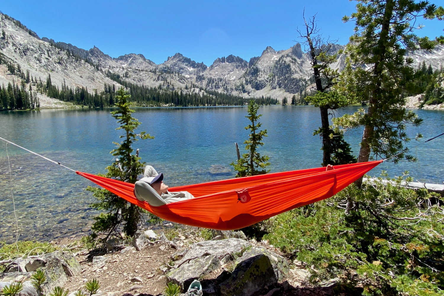 A backpacker relaxing in a red Eno Ultralight Sub6 hammock near a mountain lake in the Enchantments