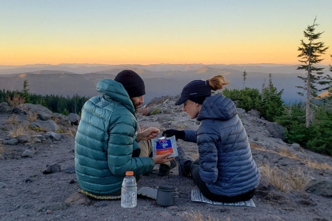 A backpacking couple sharing a freeze-dried meal at sunset on the Timberline Trail.