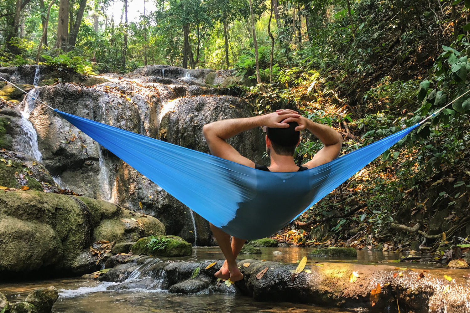 A hiker relaxing in front of a secluded waterfall in Hawaii in the Hummingbird Single hammock