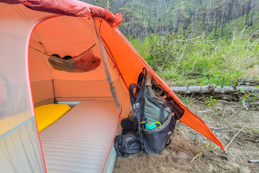 Close-up image of an orange tent set up with a backpack sitting in the vestibule.