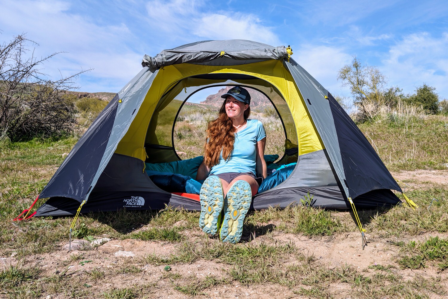 A hiker sitting in the doorway of The North Face Stormbreak 2 tent in a sunny Arizona campsite