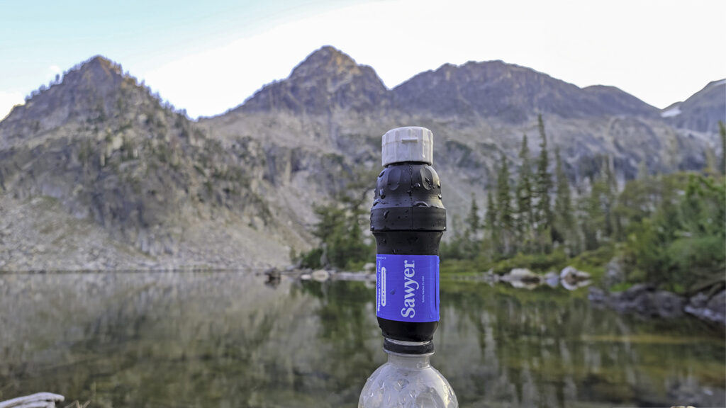 Closeup of the Sawyer Squeeze water filter in front of an alpine lake