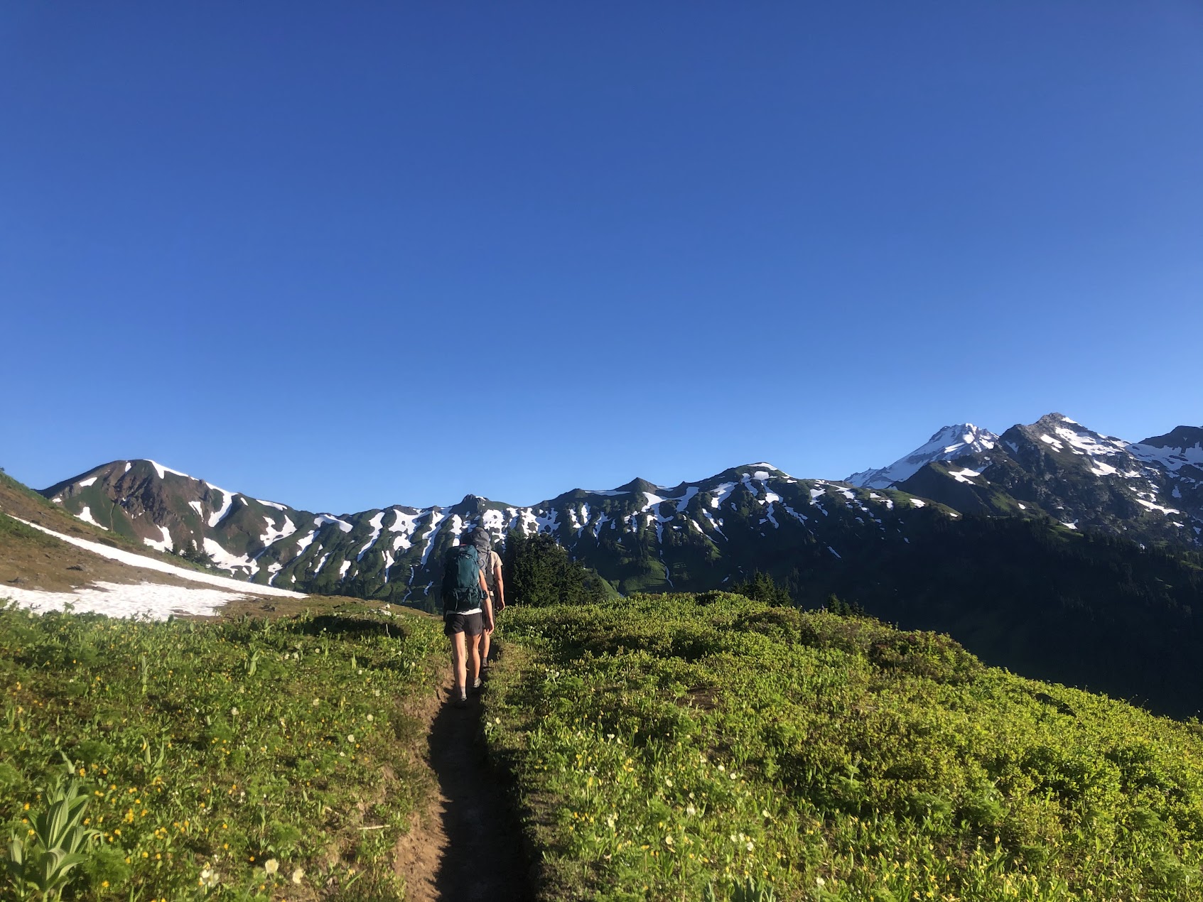 two backpackers in the alpine on a sunny day with snow dotted mountains