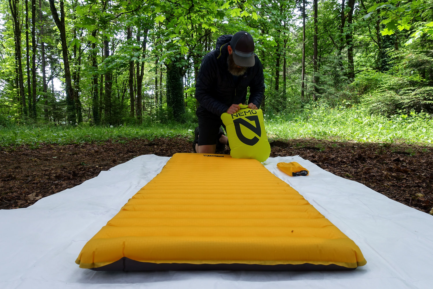 a backpacker inflating the NEMO tensor trail ultralight with a pump sack outside under a green canopy forest.