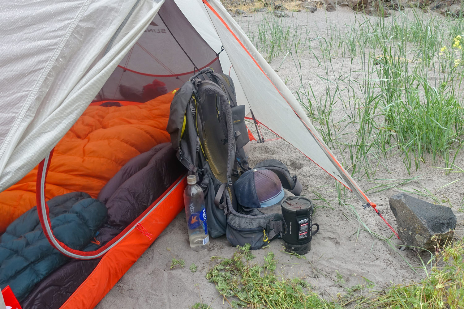 Close up of a camping tent with the fly on. A backpack is tucked inside the vestibule.