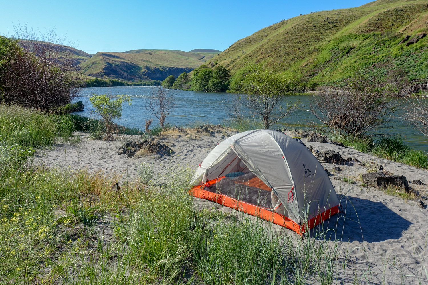 A tent is setup in a lush green valley near a lake.