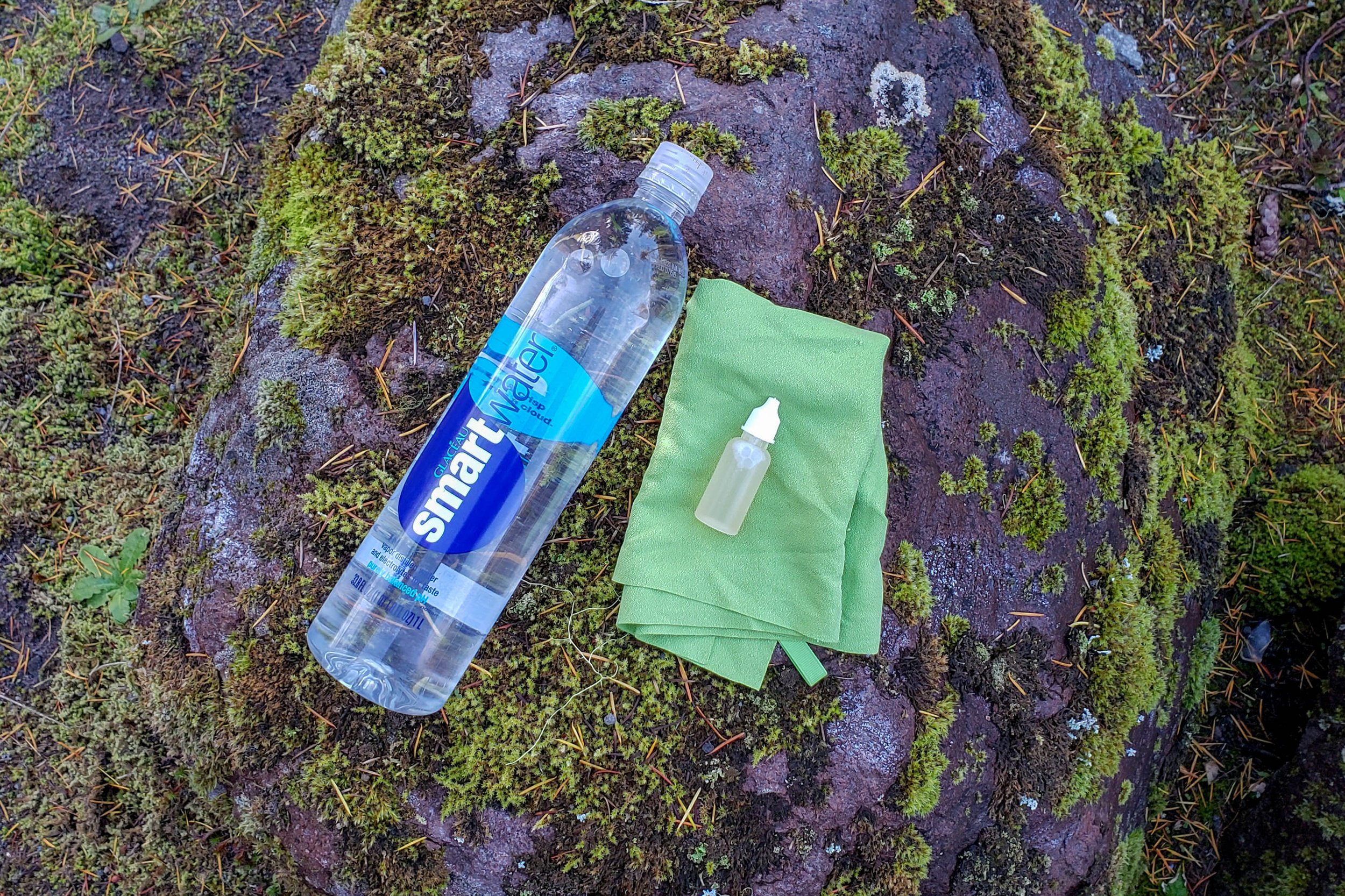 Top-down view of a water bottle, a pack towel, and a small bottle of biodegradable soap