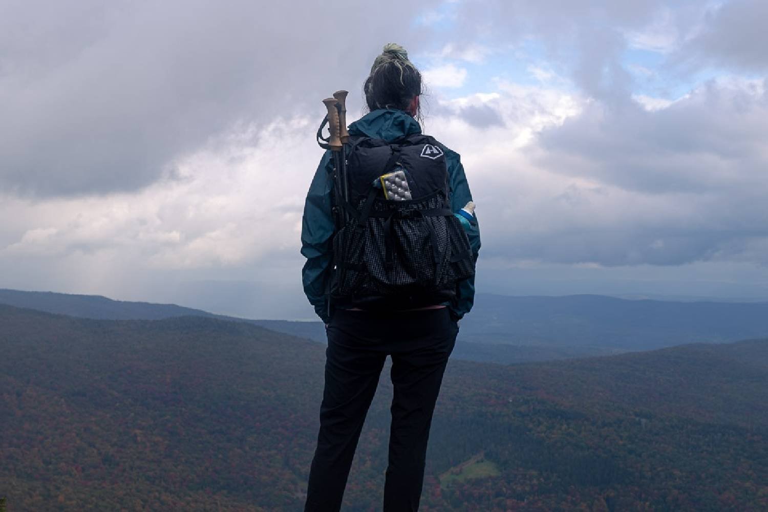 A hiker wearing the Hyperlite Mountain Gear Southwest 2400 standing on a ledge looking at a cloudy mountain view