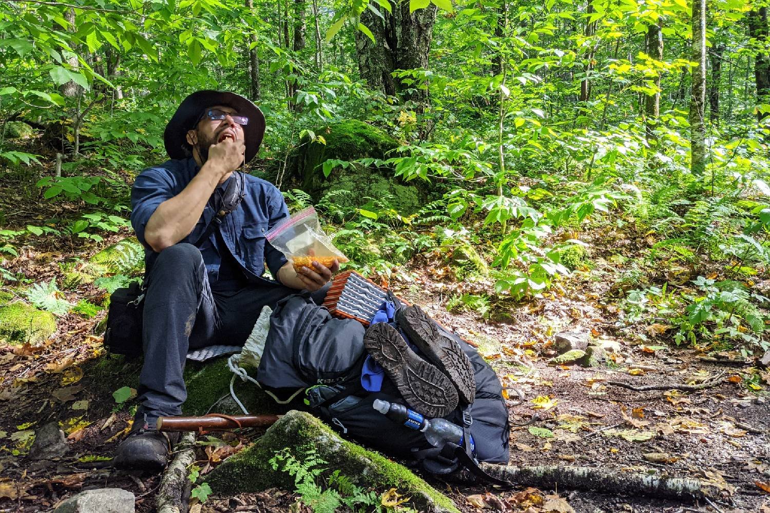 A hiker sitting on a rock eating a snack