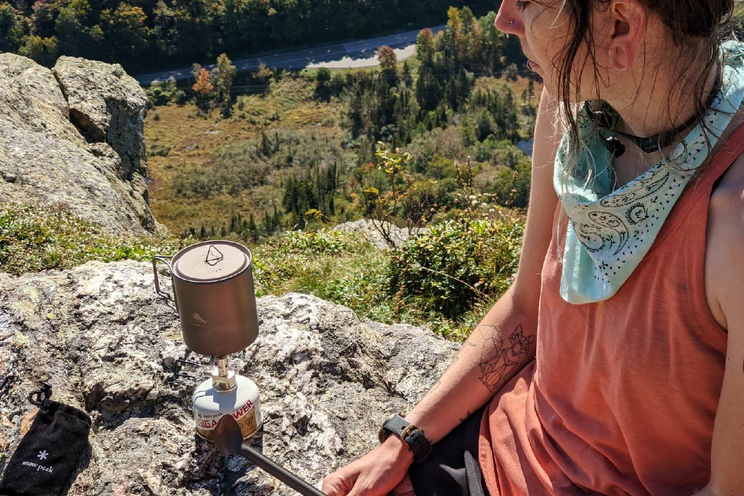 A hiker sitting on a ledge cooking on a backpacking stove