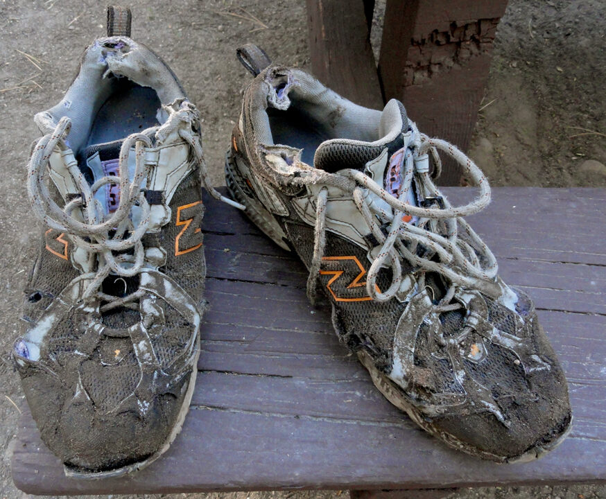 an extremely beat up and hole ridden pair of trail running shoes on a table
