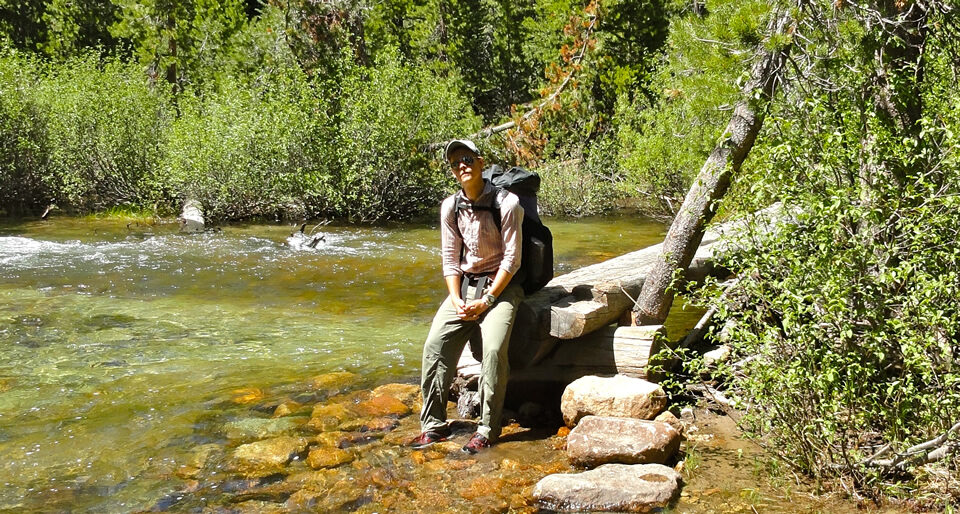 a women sits on a rock in water with a lamenting look on her face