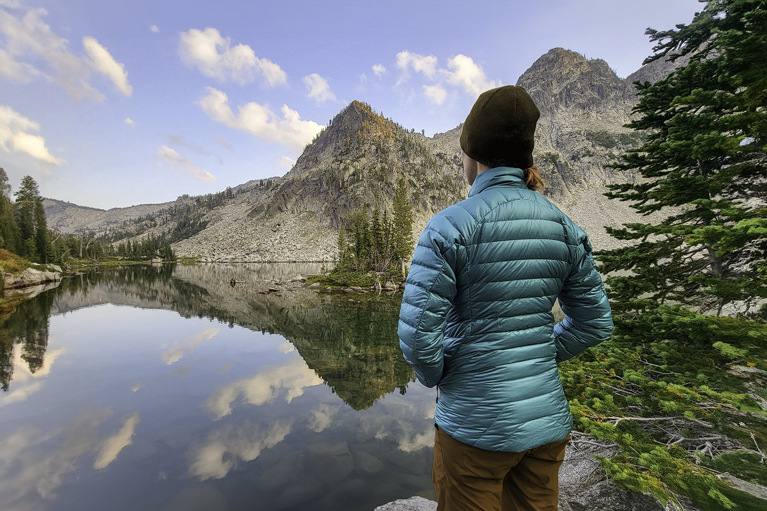 A backpacker standing by a mountain lake in a teal down jacket