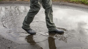 A hiker walking through a puddle in a pair of low ankle rain boots