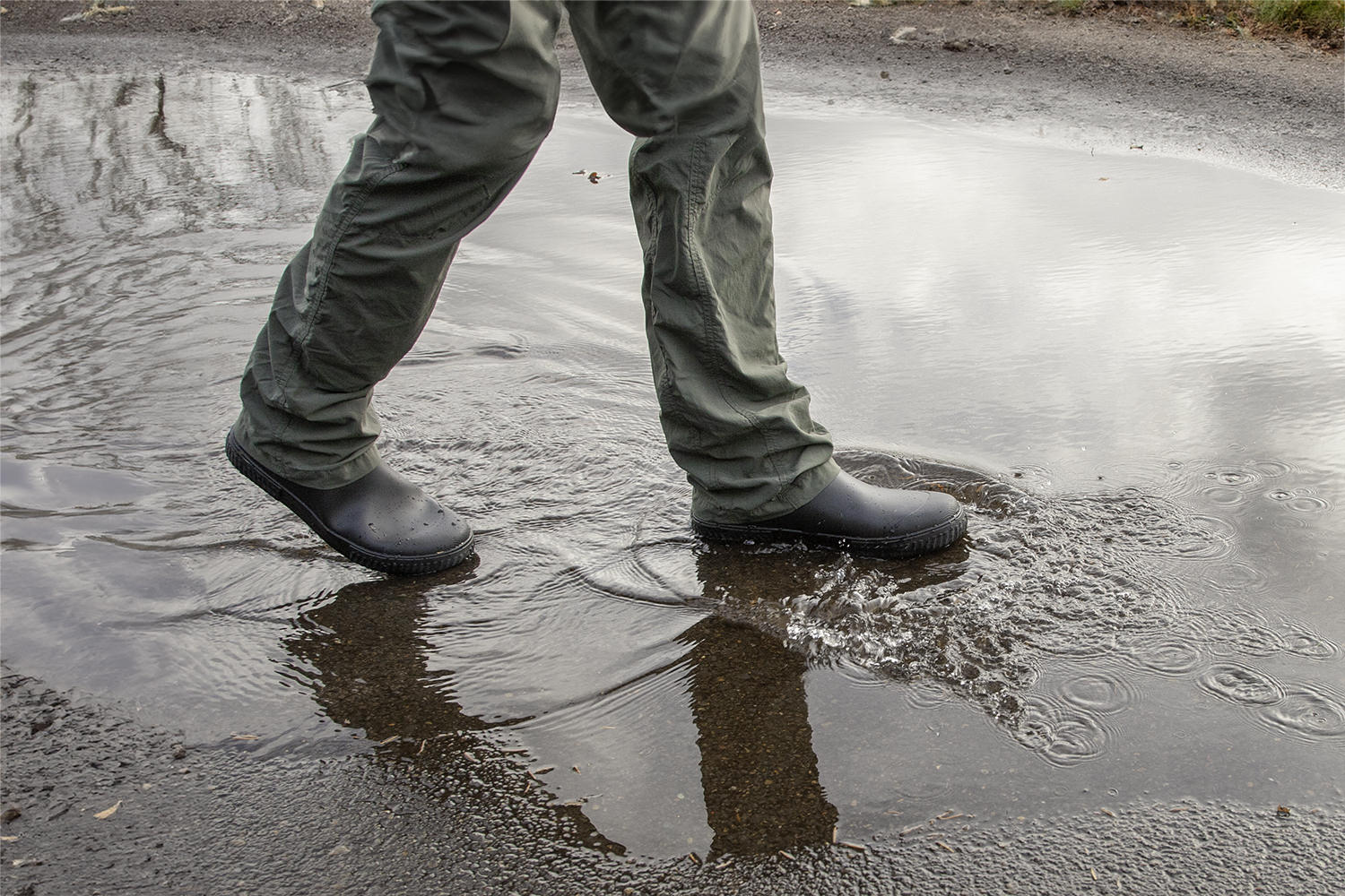 A hiker walking through a puddle in a pair of low ankle rain boots