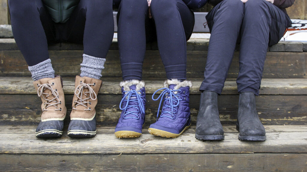 Closeup of three women's sitting on some steps in winter boots including the Sorel Slimpack III Lace & Columbia Minx Shorty III