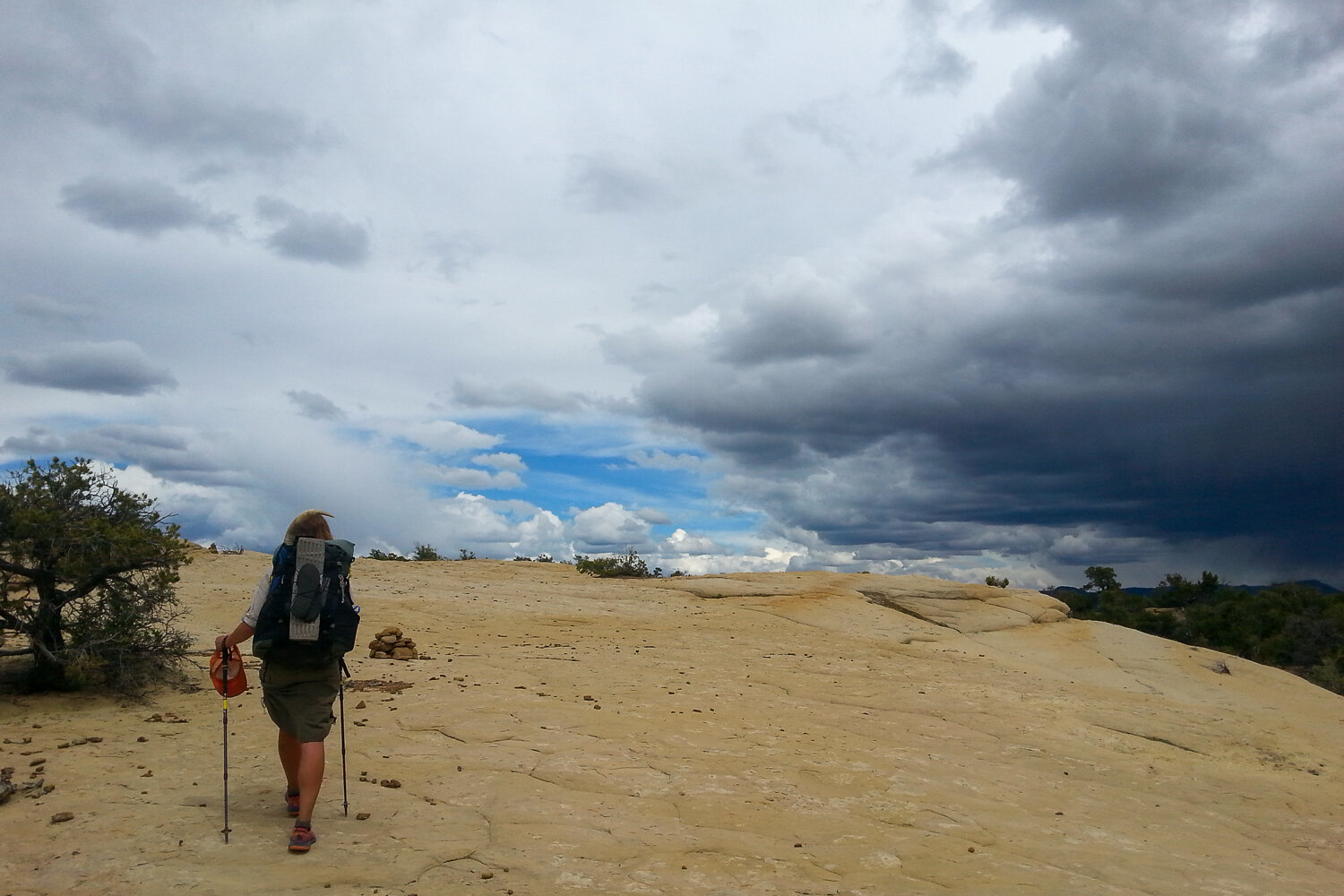 a backpacker in the desert with half of the sky clear and blue, half dark and stormy