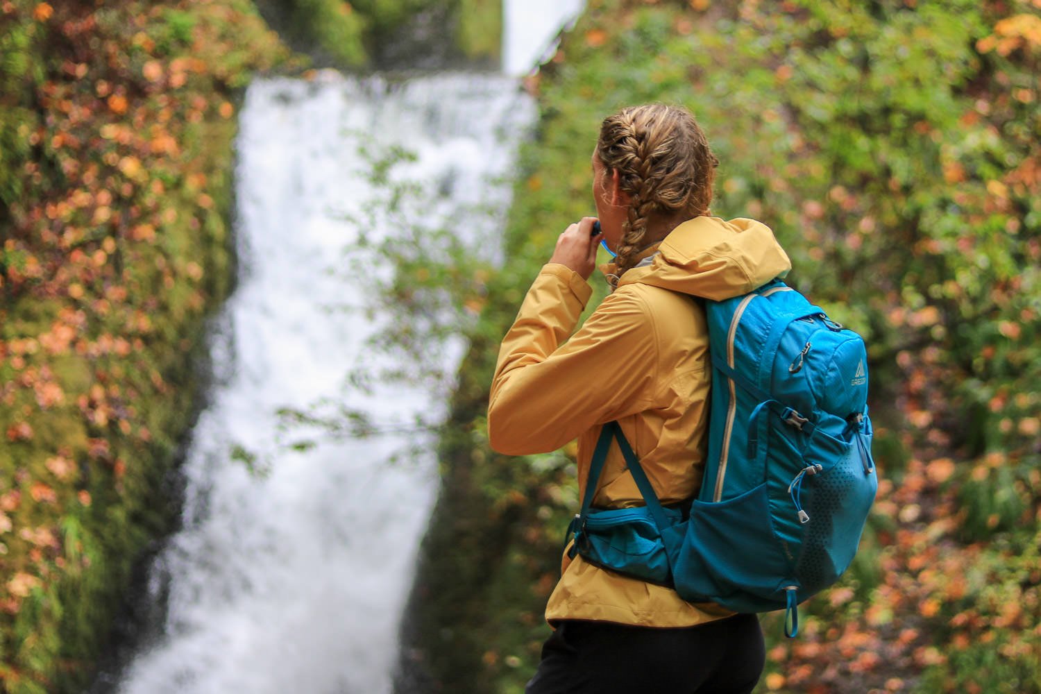A hiker drinking out of a hydration pack in front of a waterfall