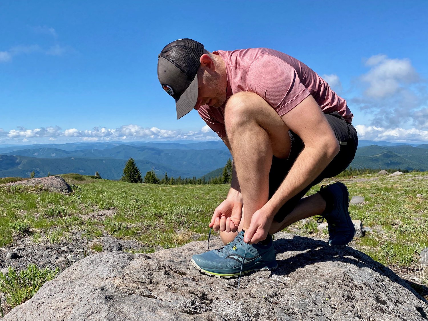 A hiker tying his shoe with an expansive valley view in the background