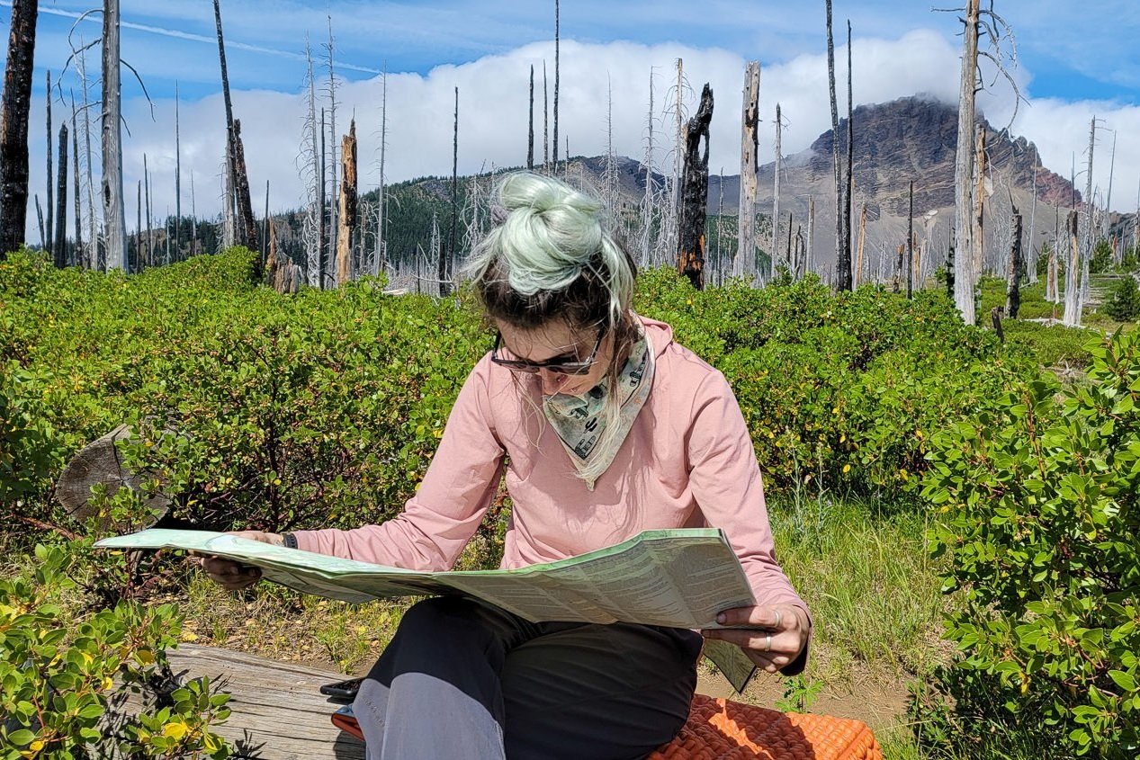 A hiker sitting on a rock looking at a map with a mountain in the background