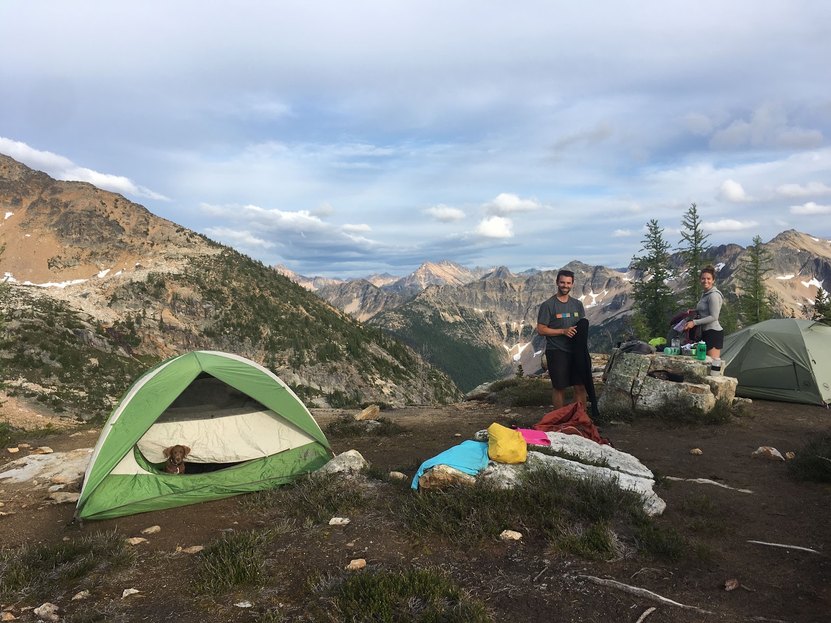 two backpackers setting up camp with a puppy poking its head out of one of the tents in the north cascades wilderness in washington