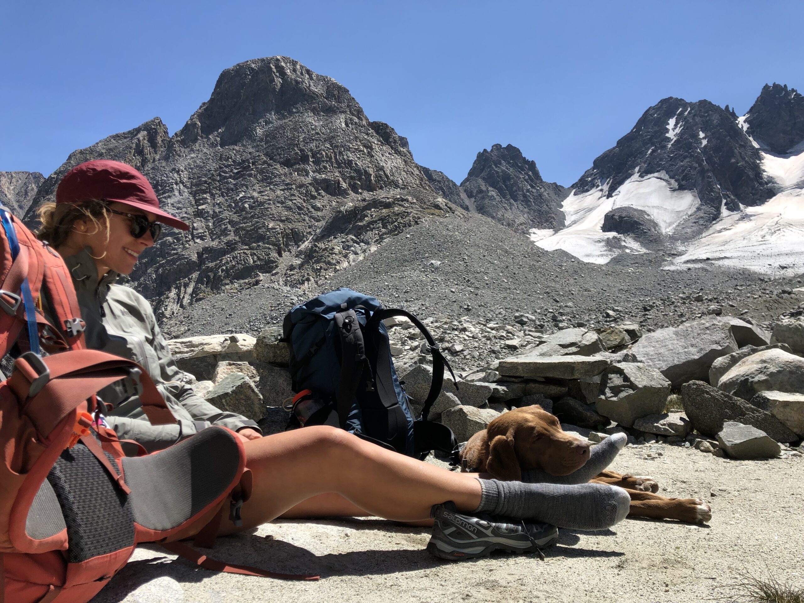 a backpacker resting on the ground with a dog resting its head on her foot in the wind river range