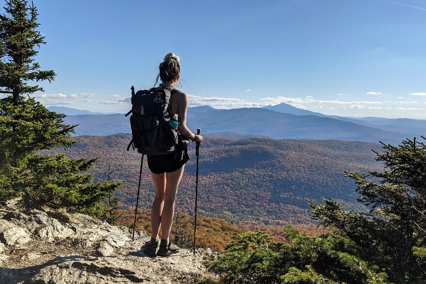 A hiker holding the Gossamer Gear LT5 trekking poles looking off at a distant mountain view