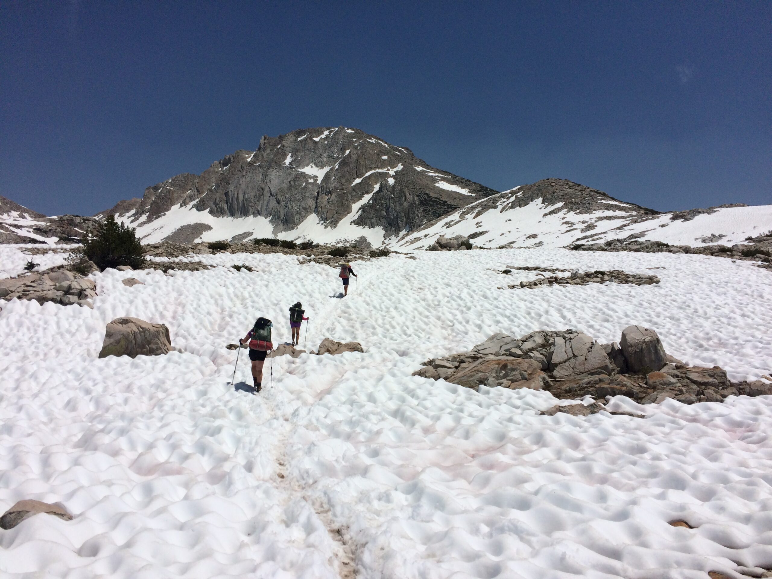backpackers crossing a snowfield with trekking poles