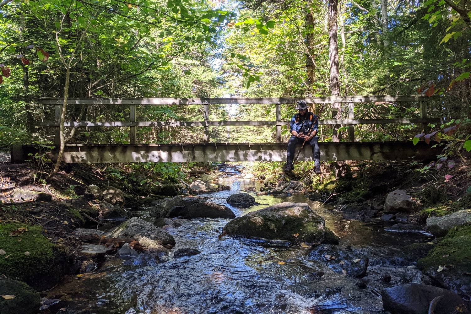 A Long Trail hiker sitting on a bridge over a stream