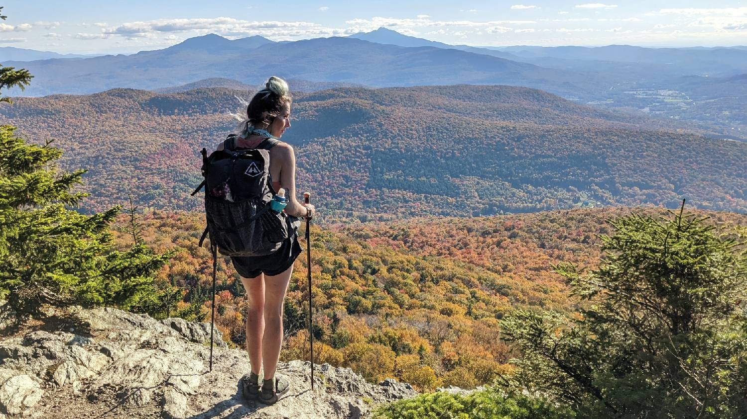 A Long Trail hiker standing on a ledge looking at a view of distant mountains