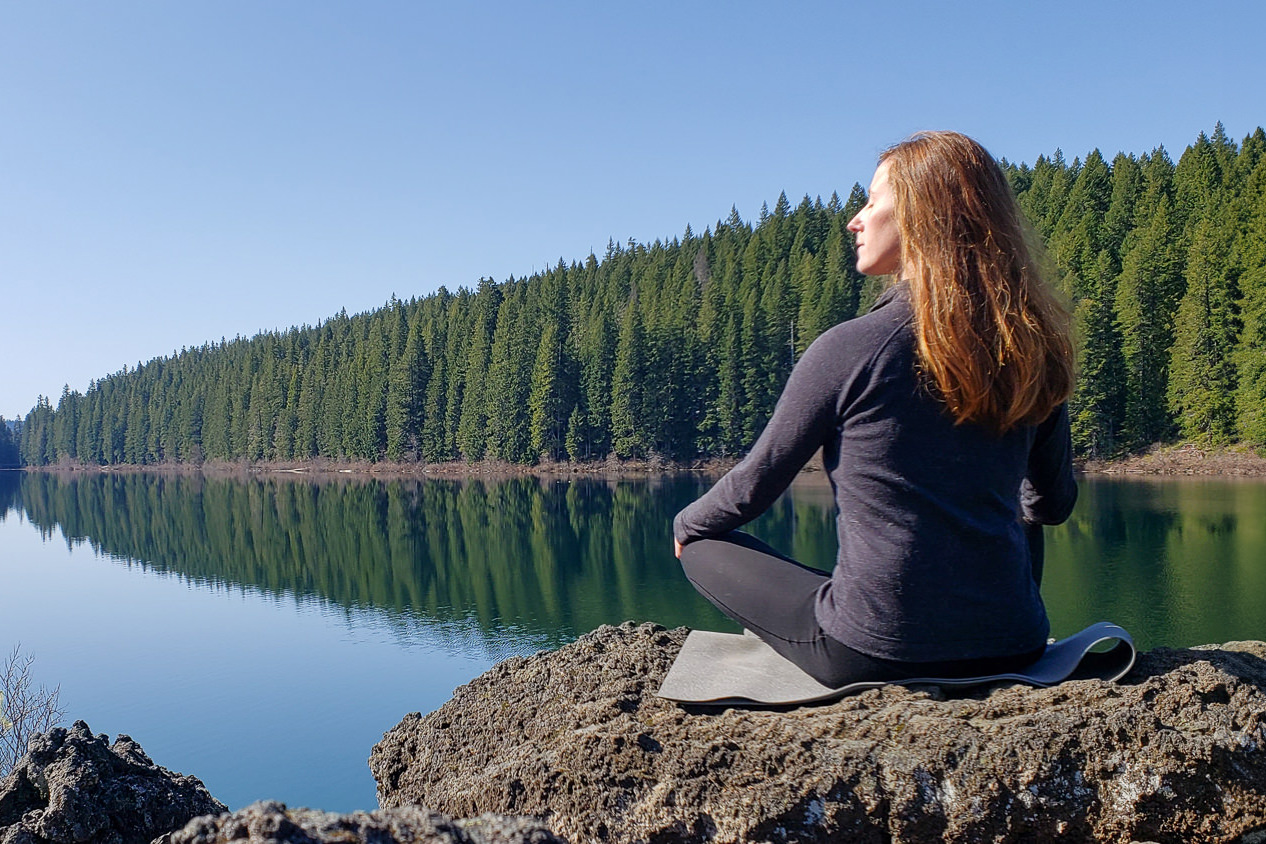 A woman sitting on the edge of a tree-lined lake in the Smartwool Classic Thermal Base Layers