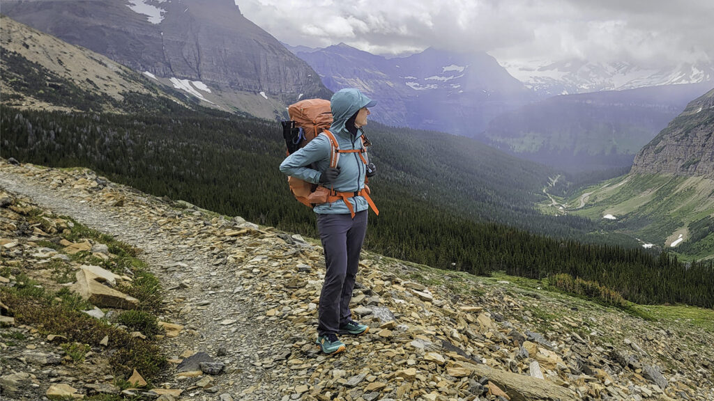 A backpacker wearing the Black Diamond Alpine Start Windbreaker while hiking in Glacier National Park in June