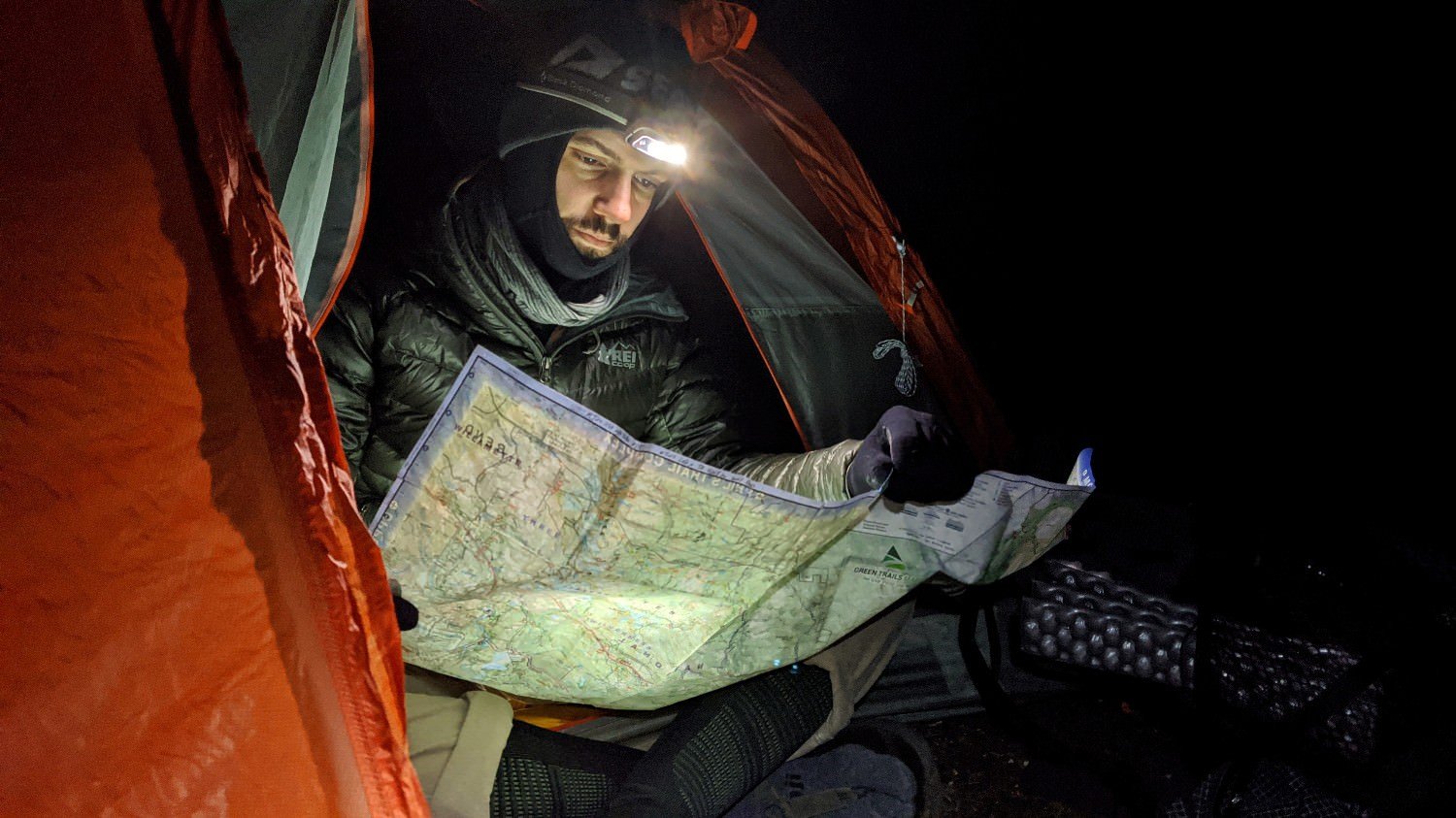 a backpacker is reading a map while bundled up seated at the door of his tent