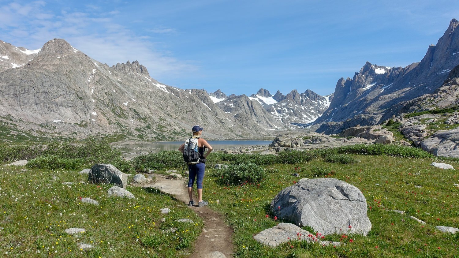 A backpacker on a trail with a lake and a big mountain view in the background