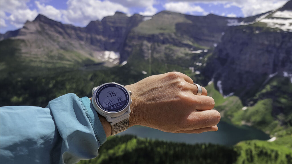 Closeup of the Coros Apex 2 GPS Watch on a backpacker's wrist with steep mountains in the background