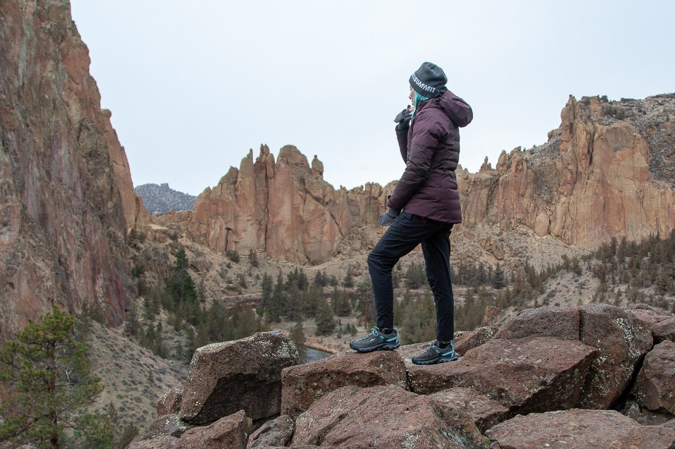 A hiker wearing the REI Stormhenge jacket standing on a ledge looking at a rocky mountain view