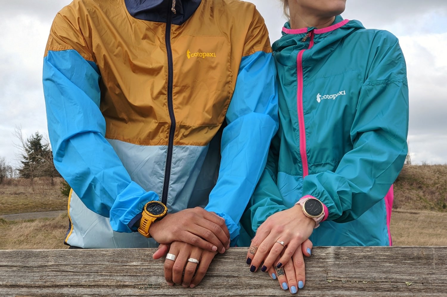 Closeup of a couple wearing windbreakers and the Garmin Instinct 2 Solar and Garmin Venu 2 GPS watches