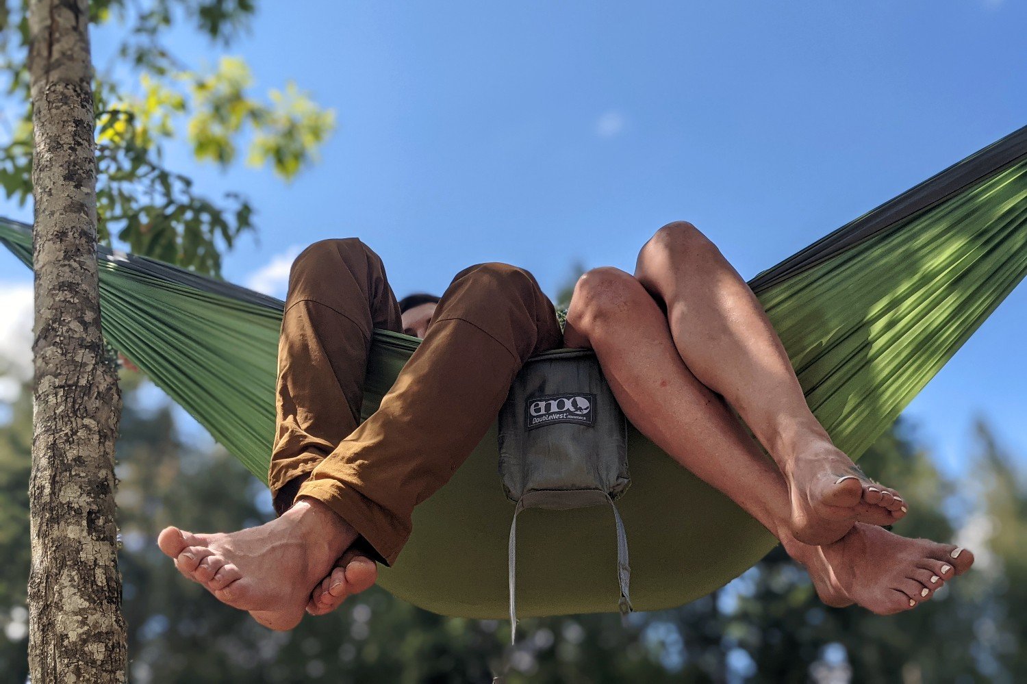 A view from below of two peoples feet hanging over the edge of the ENO Doublenest hammock