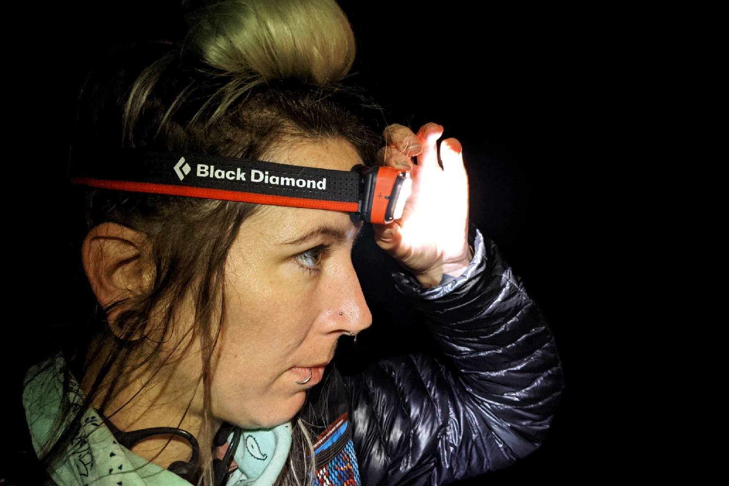 a backpacker at night with their hand on the headlamp to change the light setting