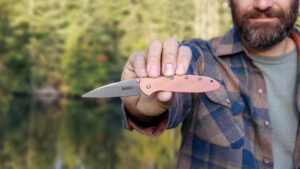 Closeup of a man holding the Kershaw Leek out in front of him with a tree-lined lake in the background