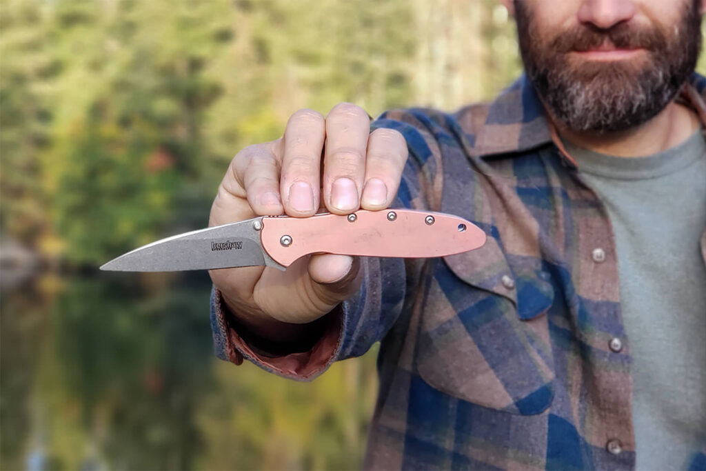 Closeup of a man holding the Kershaw Leek out in front of him with a tree-lined lake in the background