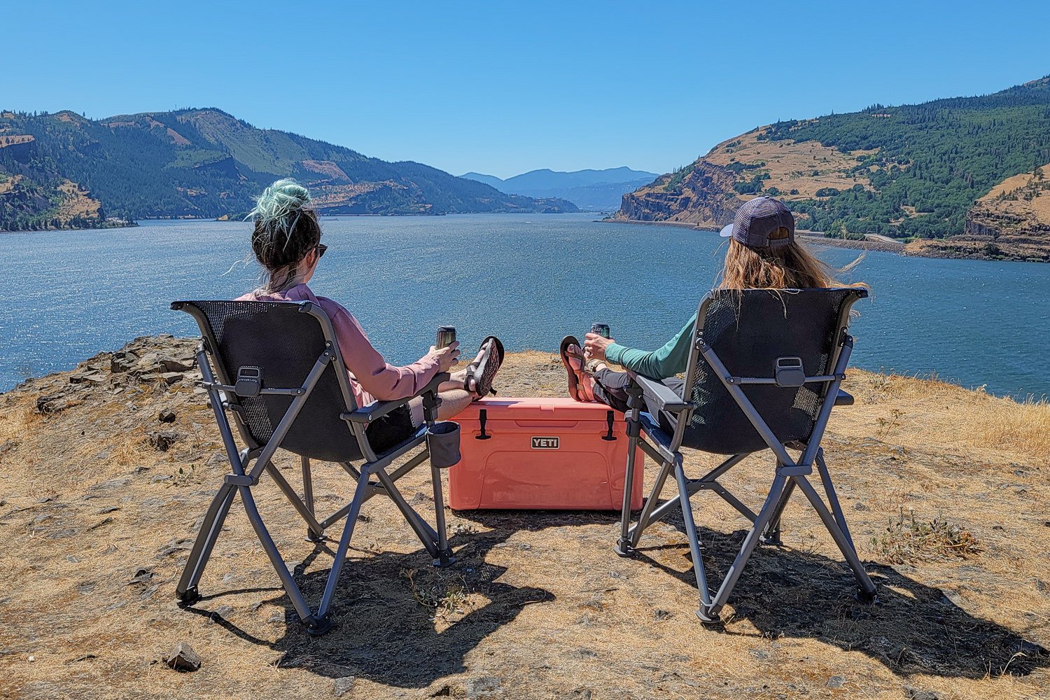 Two people sitting in Yeti Trailhead Chairs looking at a river valley view with mountains in the background