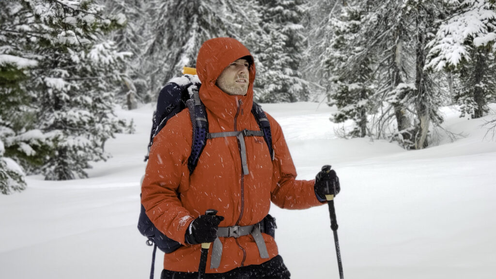 A man with a backpack wearing a red REI Stormhenge winter jacket in a snowy scene