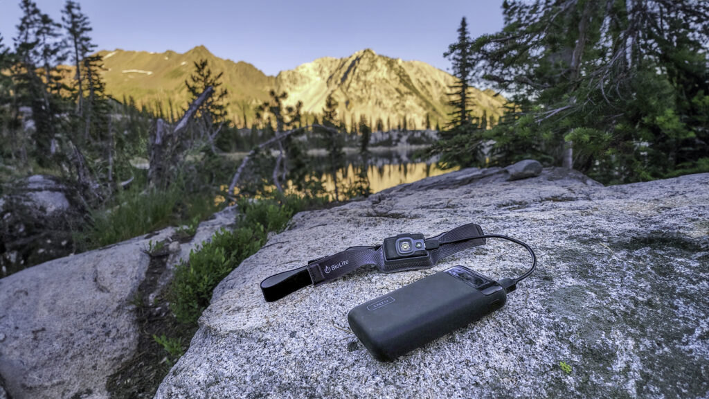 The Iniu 20000 PD power bank sitting on a granite slab while charging a rechargeable Biolite headlamp with the Wallowa Mountains at sunset in the background