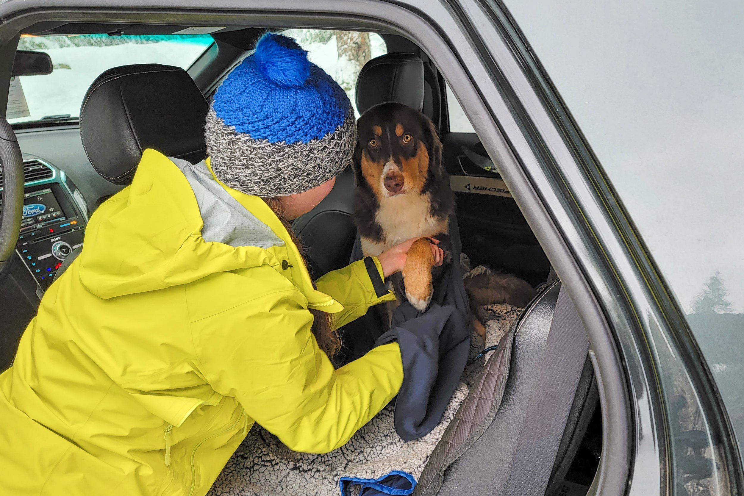 A woman drying off her dog in the car after a winter hike